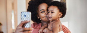 Mutter macht Seflie mit Kleinkind auf dem Arm